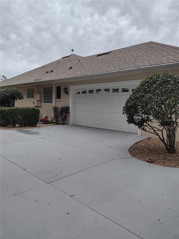 A tan house exterior features a white two-car garage door and a concrete driveway — 592 DOWLING CIRCLE, LADY LAKE, FL