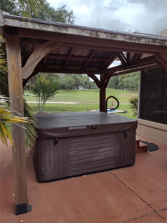 A hot tub with a cover sits under a wooden pavilion on a concrete patio — 592 DOWLING CIRCLE, LADY LAKE, FL