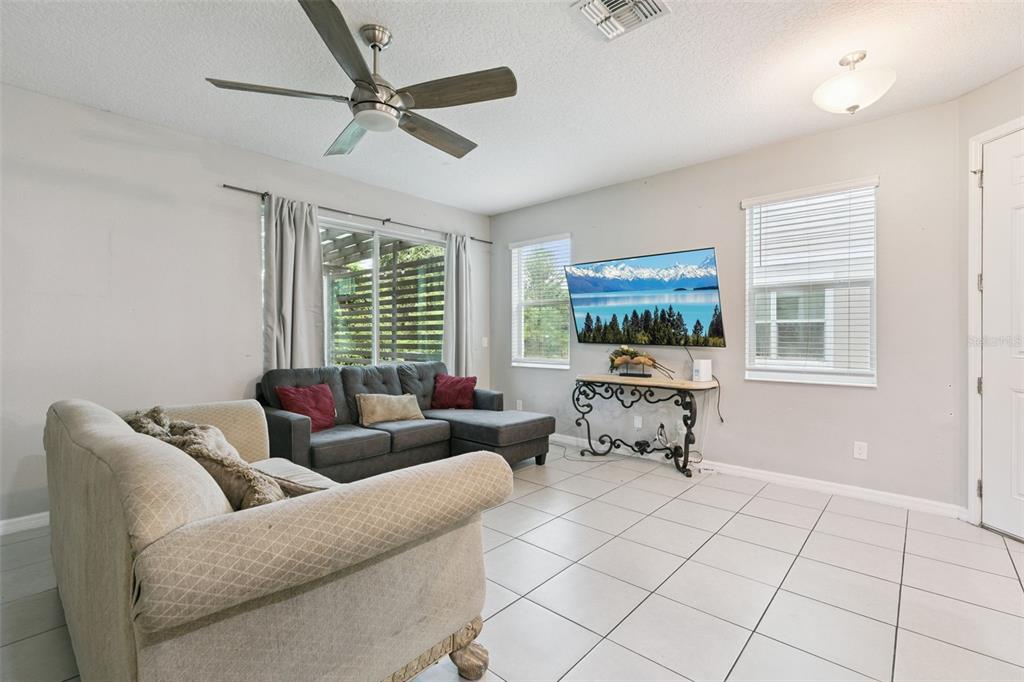 A living room features tile flooring, a ceiling fan, a sectional sofa, and a wall-mounted television — 6803 TUSSILAGO WAY, ORLANDO, FL