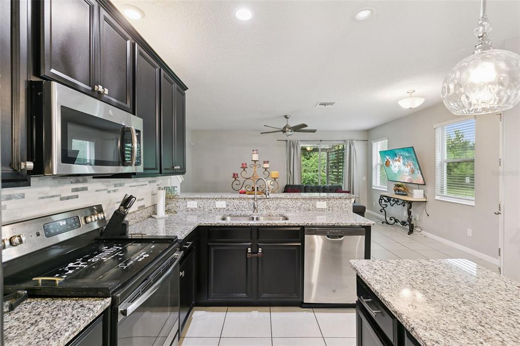 A kitchen with dark cabinets, granite countertops, stainless steel appliances, and an open living area — 6803 TUSSILAGO WAY, ORLANDO, FL