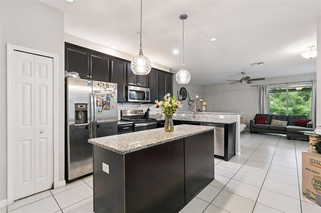A kitchen with dark cabinets, granite countertops, and an island opens into a living area — 6803 TUSSILAGO WAY, ORLANDO, FL