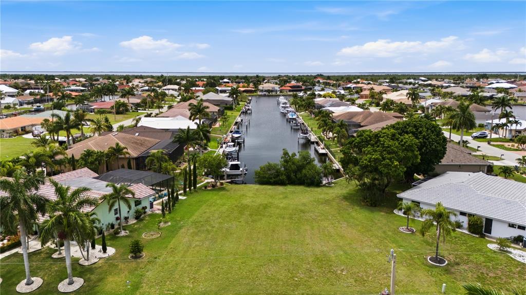 An aerial view shows a vacant grassy lot situated along a residential canal with boats — 1121 CORONADO DRIVE, PUNTA GORDA, FL
