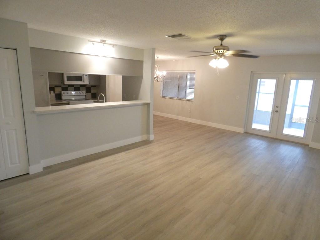 An open-concept living area features light wood-look flooring, a kitchen pass-through, and glass doors — 1024 10TH CIRCLE SE, LARGO, FL