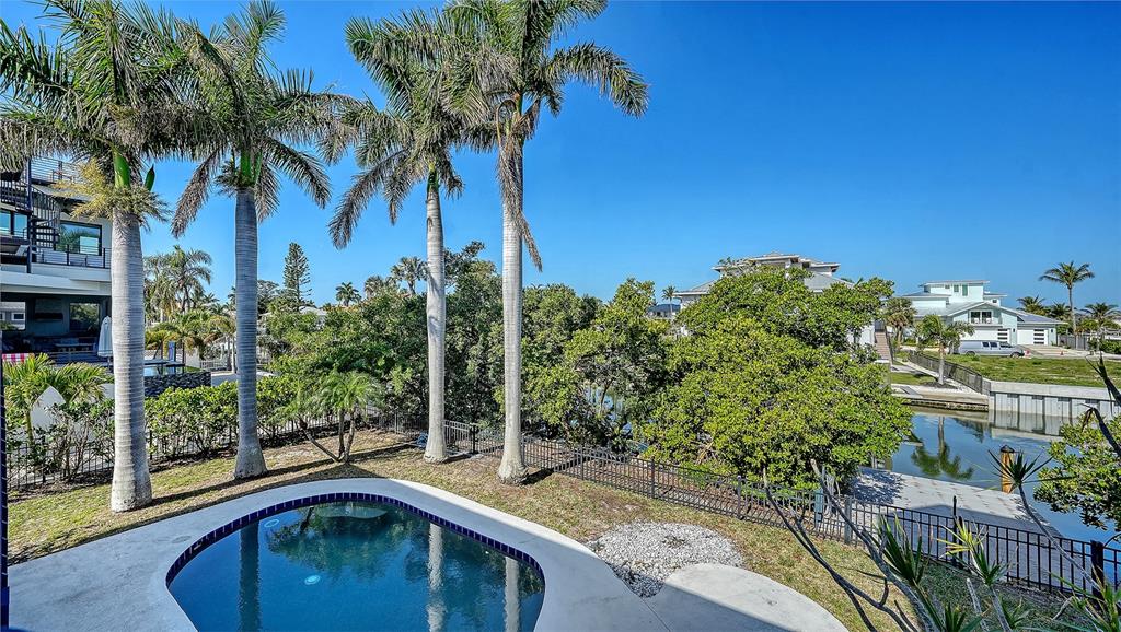 A backyard features a swimming pool, palm trees, and a canal view under a clear sky — 771 MARBURY LANE, LONGBOAT KEY, FL