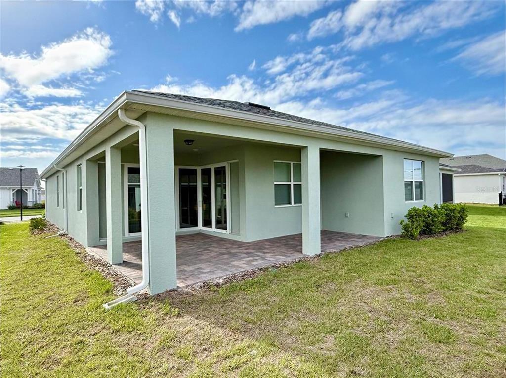 A light green house features a covered patio with paver flooring and a grassy yard — 2757 REDBLUSH TERRACE, ST CLOUD, FL