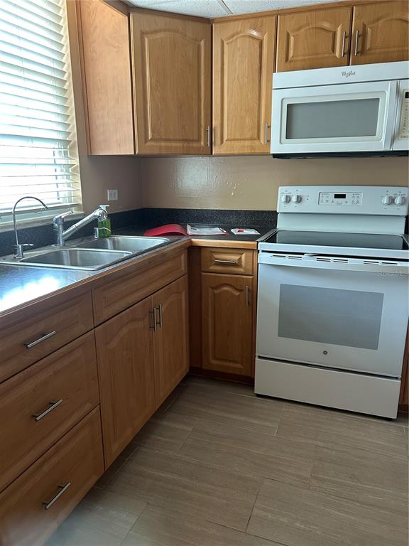 A kitchen features wood cabinets, white appliances, a dark countertop, and light-colored tile flooring — 108 CLOCKTOWER DRIVE UNIT 261, BRANDON, FL