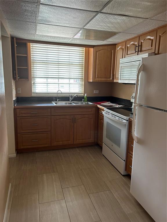 A kitchen features wood cabinets, a white refrigerator, a stainless steel sink, and tiled floors — 108 CLOCKTOWER DRIVE UNIT 261, BRANDON, FL