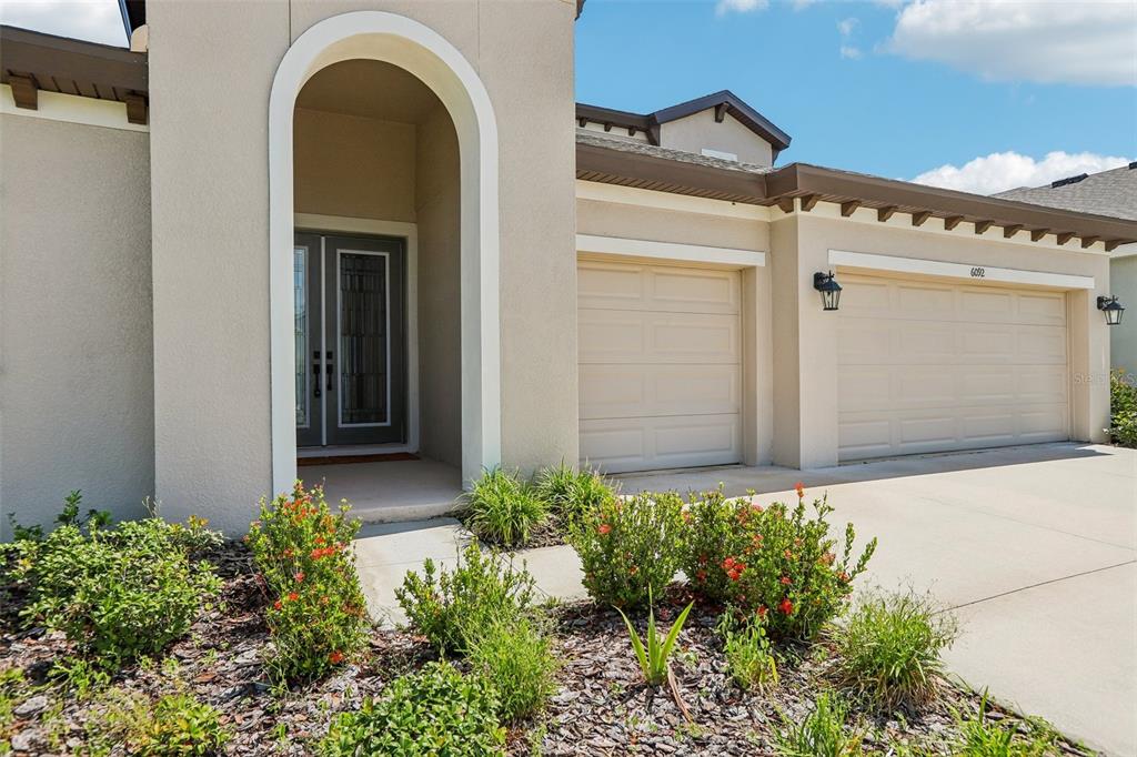 A beige house exterior features a double front door under an arch and a garage — 6092 HIDDEN BRANCH DRIVE, APOLLO BEACH, FL
