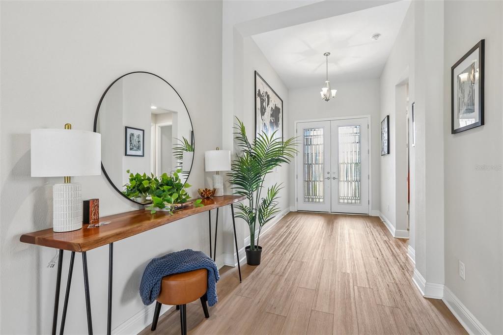 A bright entryway features a wood console table, a large round mirror, and wood-look flooring — 6092 HIDDEN BRANCH DRIVE, APOLLO BEACH, FL