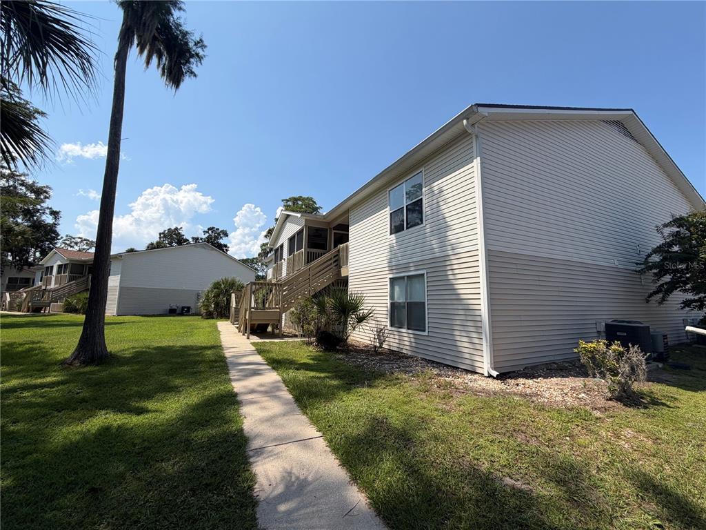 A two-story apartment building exterior with beige siding, a concrete walkway, and wooden stairs — 1600 BIG TREE ROAD UNIT A6, DAYTONA BEACH, FL