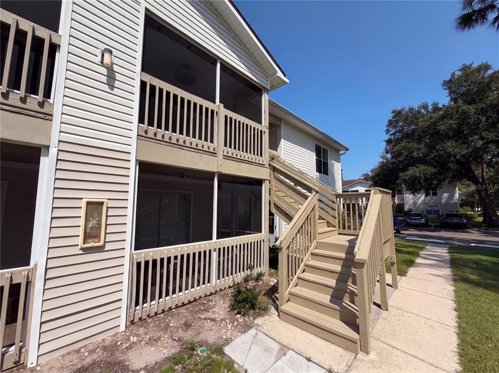 An exterior view of a two-story building featuring screened balconies and a wooden staircase — 1600 BIG TREE ROAD UNIT A6, DAYTONA BEACH, FL