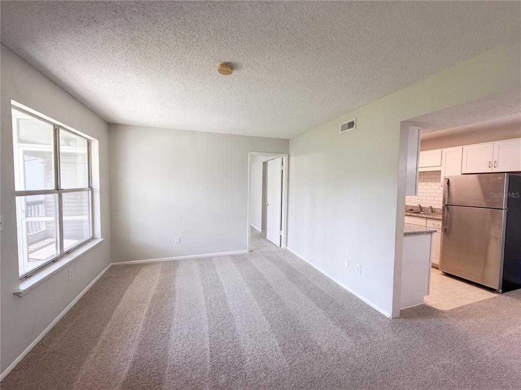 A living room with carpeted floors and a doorway leading to a kitchen with appliances — 1600 BIG TREE ROAD UNIT A6, DAYTONA BEACH, FL