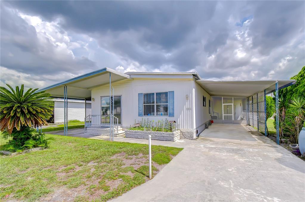 A white mobile home with a carport, covered porch, and a concrete driveway under cloudy skies — 35144 ADA AVENUE, ZEPHYRHILLS, FL