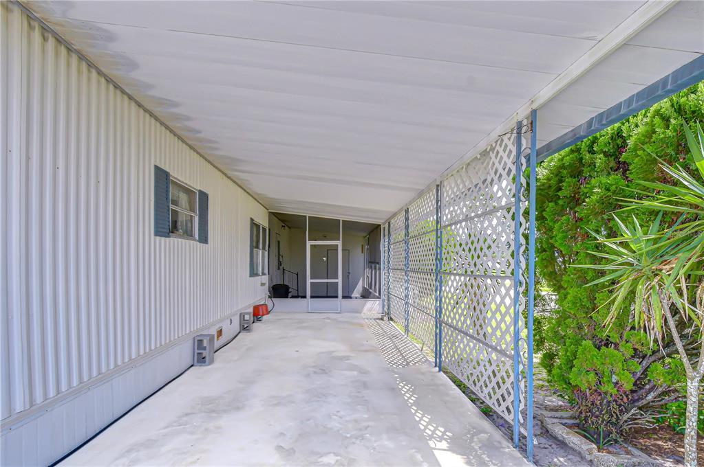 A covered concrete carport features white metal siding, lattice privacy screens, and a screened-in porch — 35144 ADA AVENUE, ZEPHYRHILLS, FL