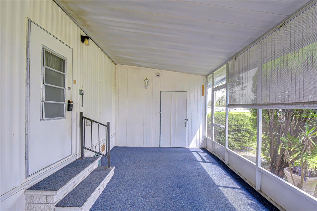 A covered porch with blue carpeting, white paneled walls, a screen enclosure, and two doors — 35144 ADA AVENUE, ZEPHYRHILLS, FL