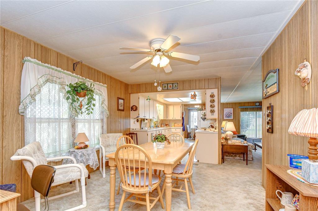 A dining area with wood-paneled walls, a ceiling fan, and an open view into the kitchen — 35144 ADA AVENUE, ZEPHYRHILLS, FL