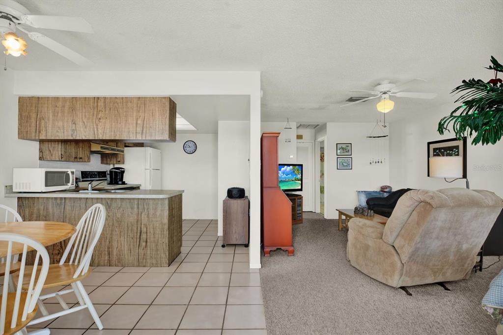 A kitchen with wood cabinets and a tile floor opens into a carpeted living room — 315 58TH STREET UNIT D, HOLMES BEACH, FL