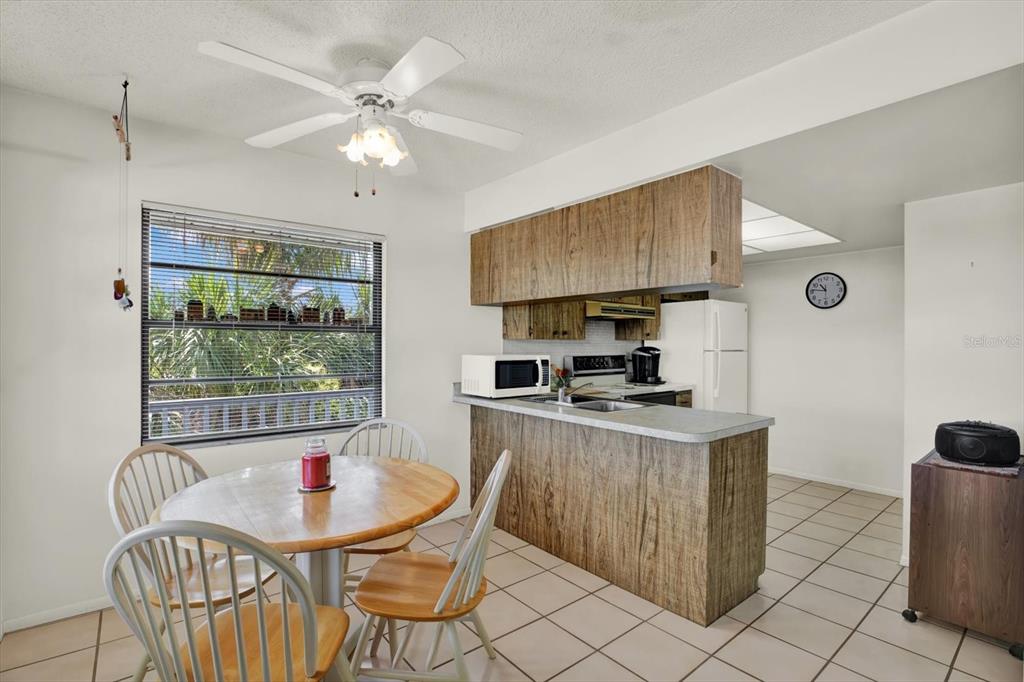 A dining area with a round wooden table sits adjacent to a kitchen with wood-grain cabinets — 315 58TH STREET UNIT D, HOLMES BEACH, FL
