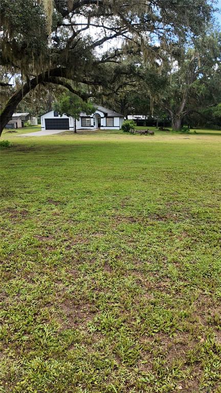 A white house with a black garage door sits on a large, grassy lot — 26348 CROOKED TREE LANE, BROOKSVILLE, FL