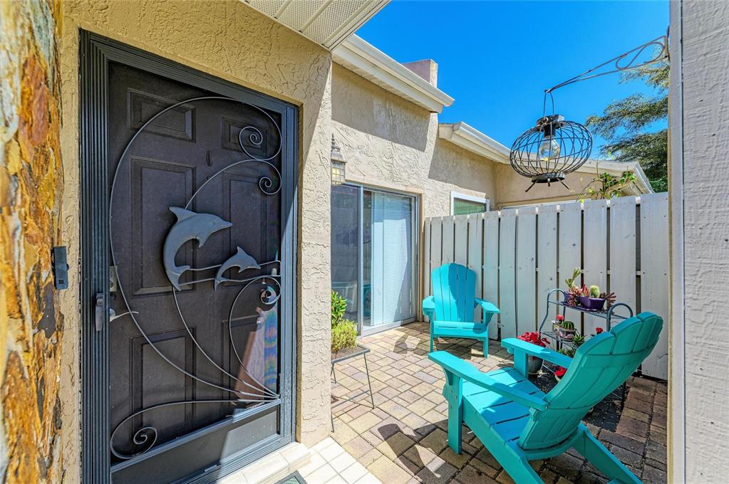 A small brick patio features two bright blue Adirondack chairs and a metal plant stand — 3405 TALLYWOOD LANE UNIT 7130, SARASOTA, FL