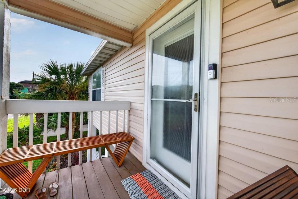 A wooden bench sits on a covered porch with beige siding and a glass door — 124 AVALON DRIVE, ORMOND BEACH, FL