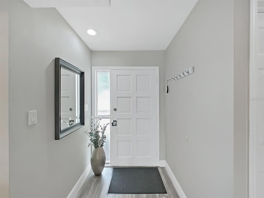 An entryway features light gray walls, wood-look flooring, a white front door, and a wall mirror — 433 S PAULA DRIVE UNIT 18, DUNEDIN, FL