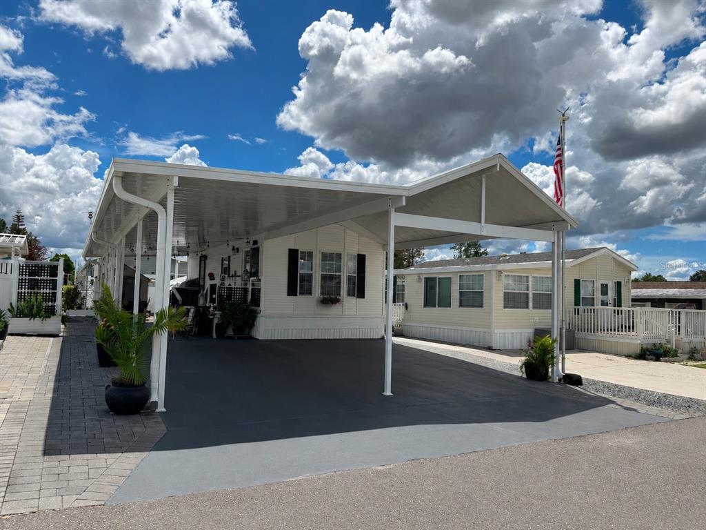A manufactured home with a large covered carport and a paved driveway under a cloudy sky — 127 TULIP STREET, DAVENPORT, FL