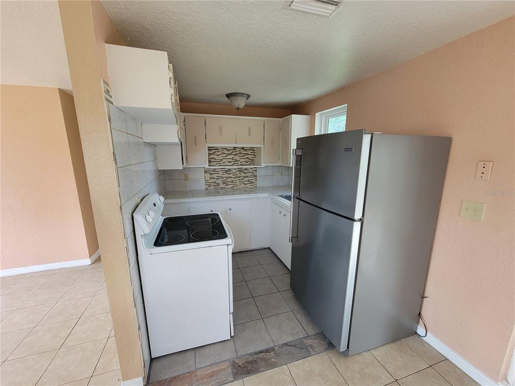 A kitchen features white cabinets, a stainless steel refrigerator, a white stove, and tiled flooring — 14297 SW 39TH TERRACE, OCALA, FL