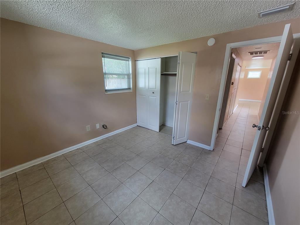 A bedroom with beige walls, tile flooring, a closet, and an open doorway to a hallway — 14297 SW 39TH TERRACE, OCALA, FL