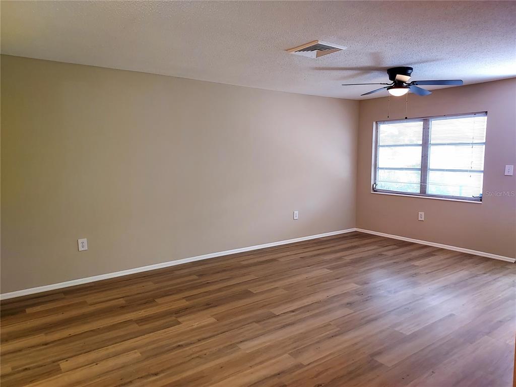 An empty room features light brown walls, wood-look flooring, a ceiling fan, and a window — 6064 ARLENE WAY UNIT 6064, BRADENTON, FL