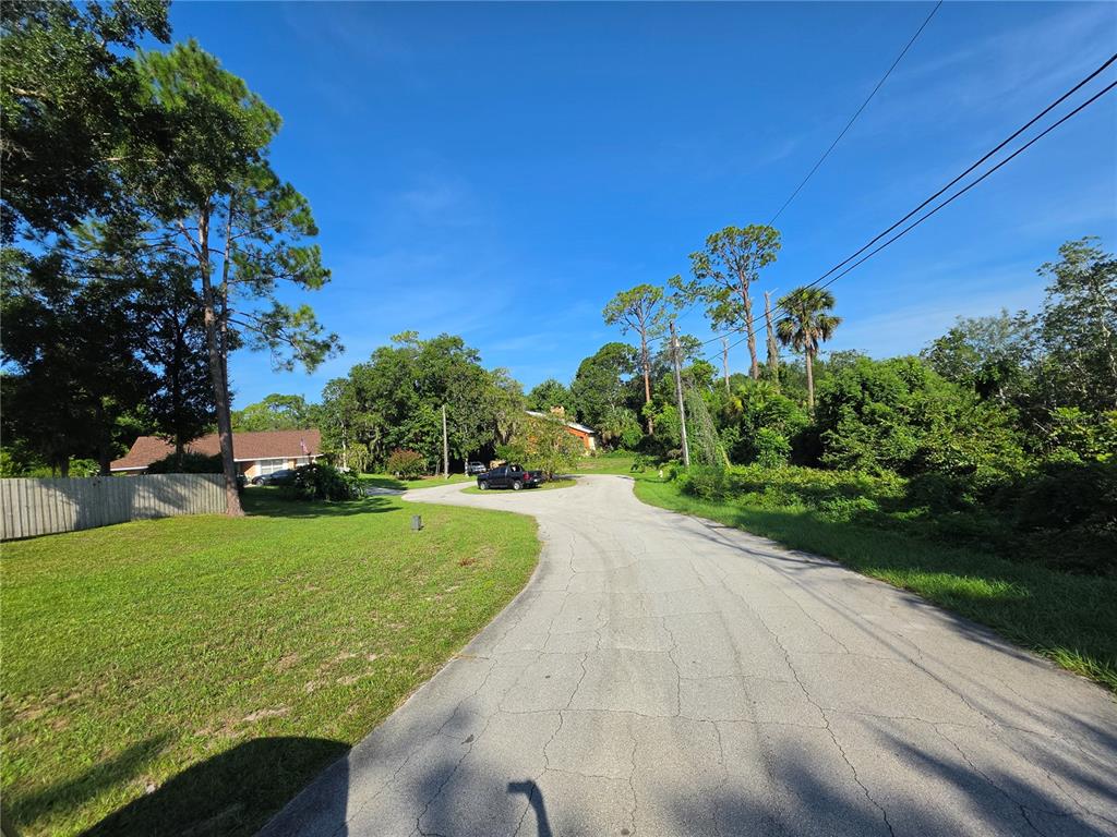 A paved road curves through a residential area with trees, grass, and a parked truck — 1792 PACO COURT, DELTONA, FL