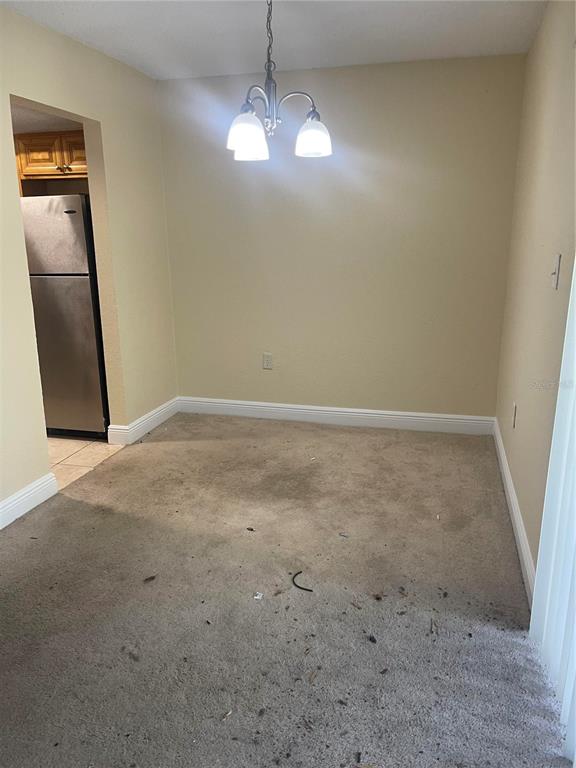 A dining area with beige carpet, tan walls, and a three-light chandelier fixture — 4769 S TEXAS AVENUE UNIT D, ORLANDO, FL