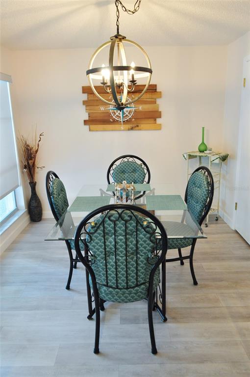 A dining room features a glass-topped table, four patterned chairs, and a spherical chandelier — 317 REX PLACE UNIT G, MADEIRA BEACH, FL