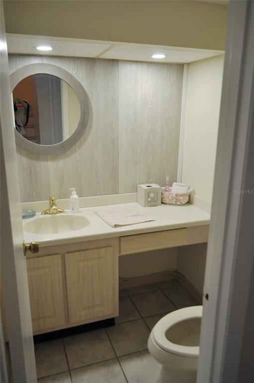A bathroom features a vanity with a light wood cabinet, round mirror, and tile flooring — 317 REX PLACE UNIT G, MADEIRA BEACH, FL
