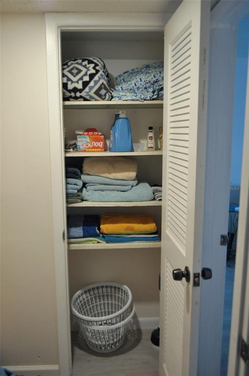 A closet with shelves holding folded towels, linens, and cleaning supplies above a laundry basket — 317 REX PLACE UNIT G, MADEIRA BEACH, FL
