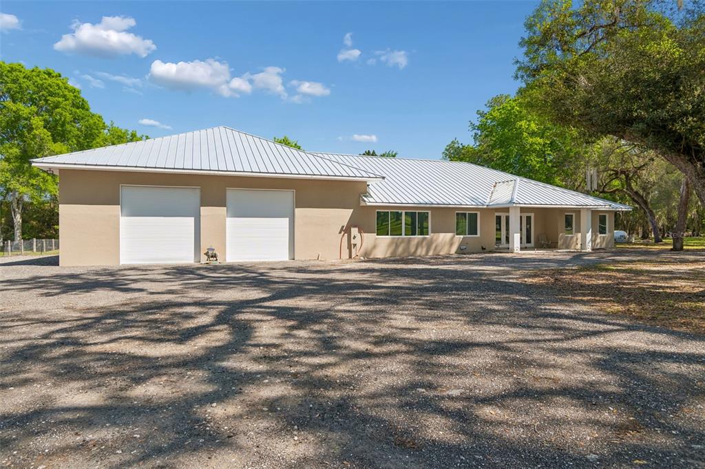 A tan house with a metal roof and two garage doors sits on a gravel lot — 4300 CR 673, BUSHNELL, FL