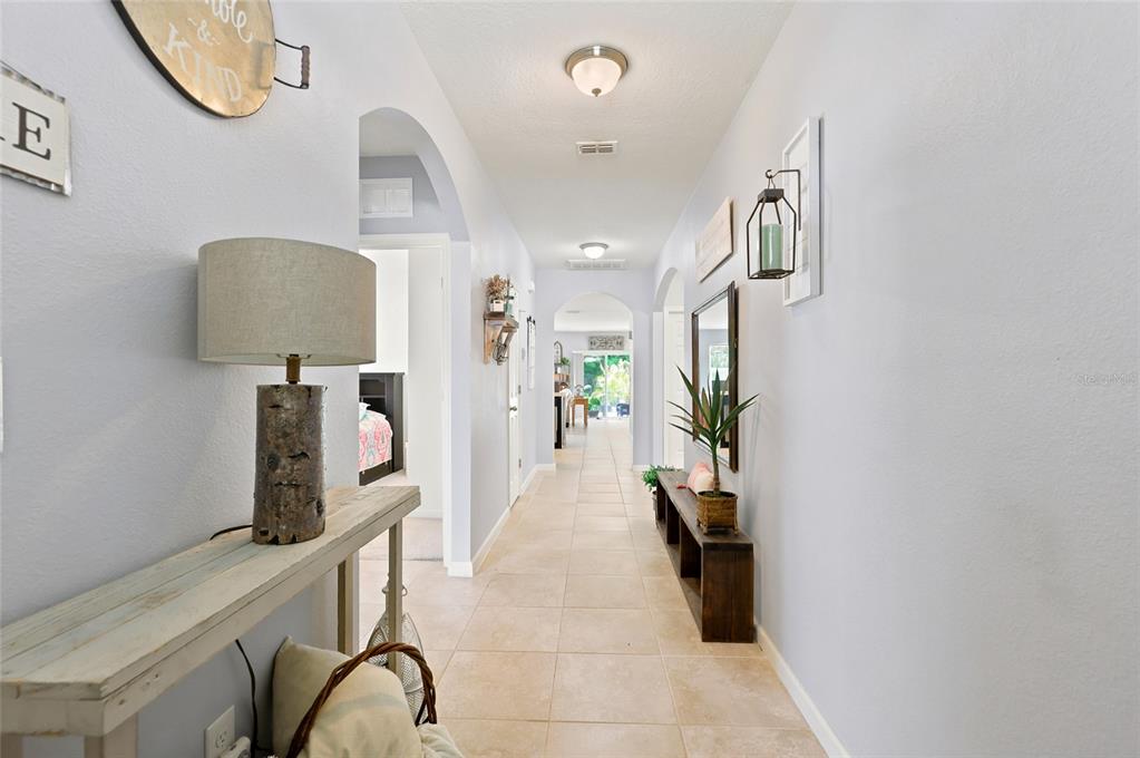 A long, tiled hallway features arched doorways, light blue walls, and two wooden console tables — 2096 SW LEAFY ROAD, PORT ST LUCIE, FL