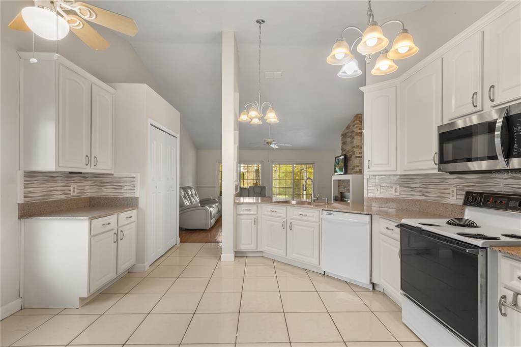 A kitchen with white cabinets, stainless steel appliances, and tile flooring opens to a living area — 3236 TIMUCUA CIRCLE, ORLANDO, FL