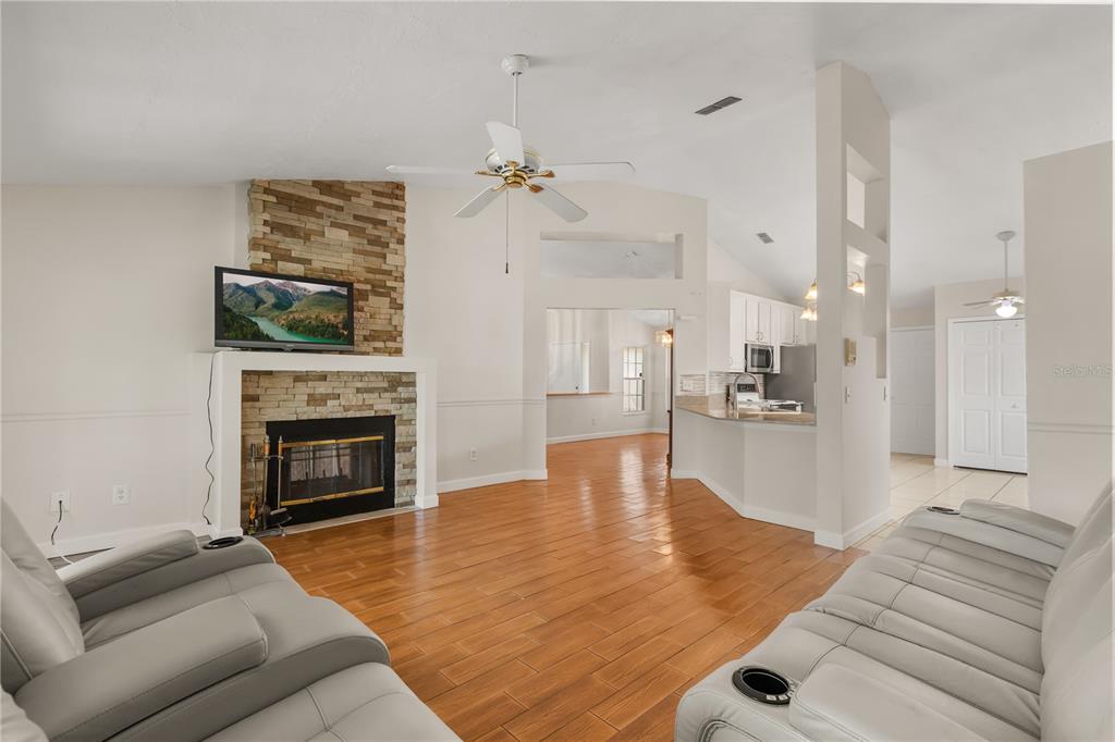 A living room with wood-look tile floors, a stone fireplace, and an adjacent open kitchen — 3236 TIMUCUA CIRCLE, ORLANDO, FL