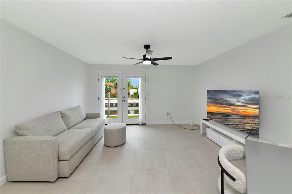 A living room features a light gray sofa, a television on a white stand, and glass doors — 729 SAINT JUDES DRIVE S UNIT 2, LONGBOAT KEY, FL