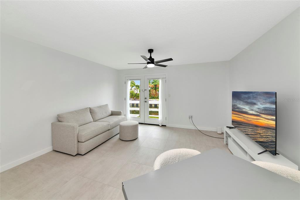 A living room features light tile flooring, a beige sofa, and glass doors to a balcony — 729 SAINT JUDES DRIVE S UNIT 2, LONGBOAT KEY, FL