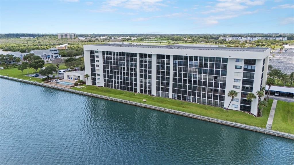An aerial view of a multi-story apartment building situated along a waterfront with a pool — 300 S SYKES CREEK PARKWAY UNIT 105, MERRITT ISLAND, FL