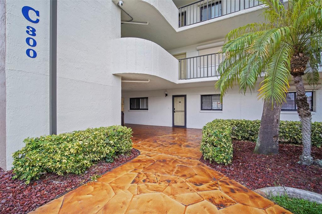 A ground-level view of a multi-story apartment building exterior with a stamped concrete walkway — 300 S SYKES CREEK PARKWAY UNIT 105, MERRITT ISLAND, FL