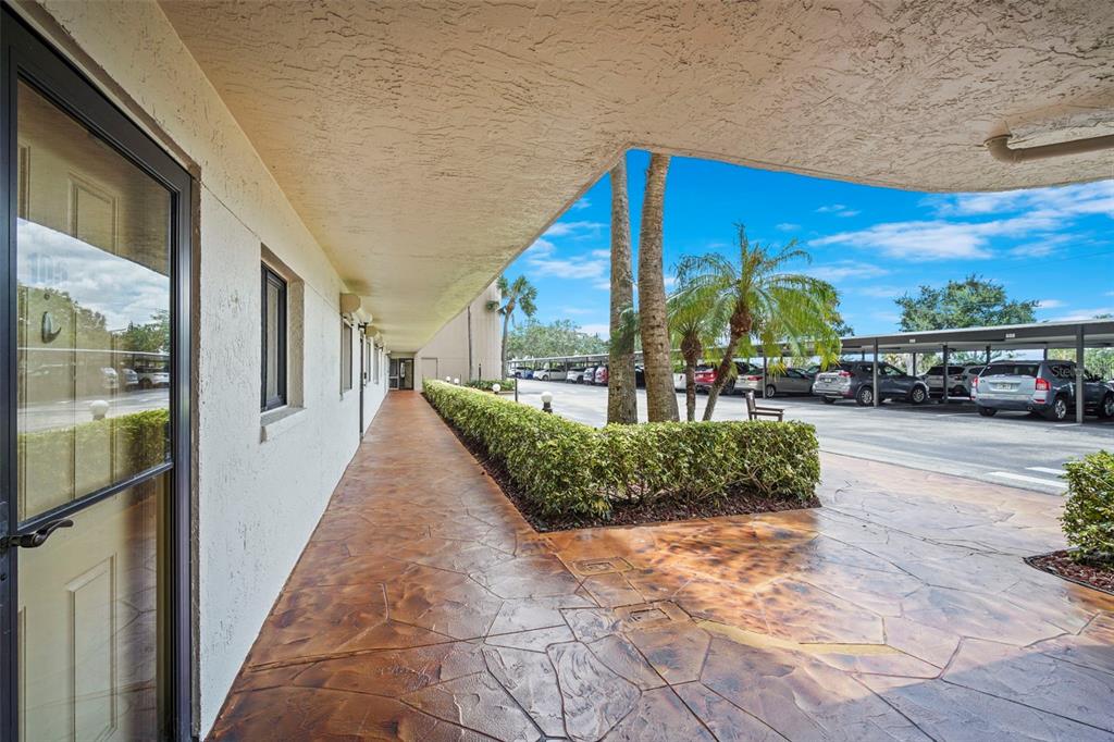 A covered walkway with stamped concrete flooring leads past a building entrance toward a parking lot — 300 S SYKES CREEK PARKWAY UNIT 105, MERRITT ISLAND, FL