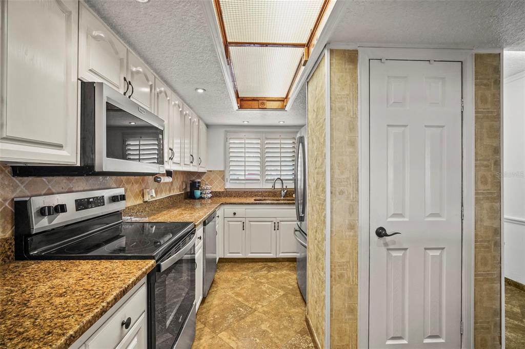 A galley kitchen features white cabinets, granite countertops, tile flooring, and a recessed ceiling light — 300 S SYKES CREEK PARKWAY UNIT 105, MERRITT ISLAND, FL