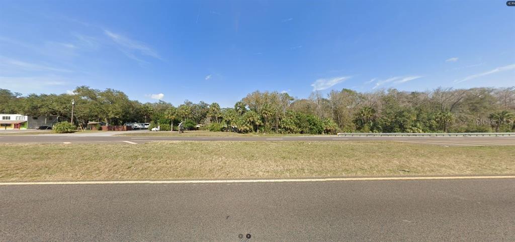 A view of a grassy roadside lot with trees and a building in the distance — E COLONIAL DRIVE, ORLANDO, FL