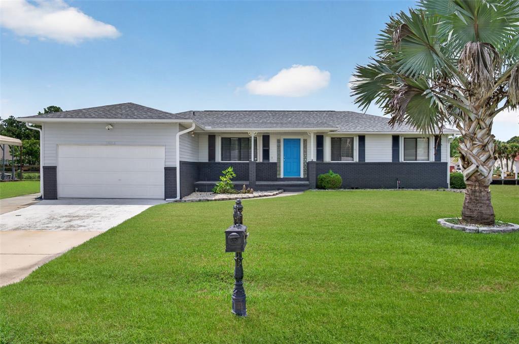 A single-story house with a white and dark gray exterior, a blue door, and a palm tree — 1613 JUNO TRAIL, ASTOR, FL