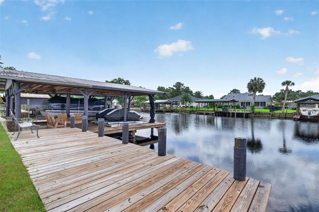 A wooden boat dock with a covered slip sits along a canal near residential homes — 1613 JUNO TRAIL, ASTOR, FL