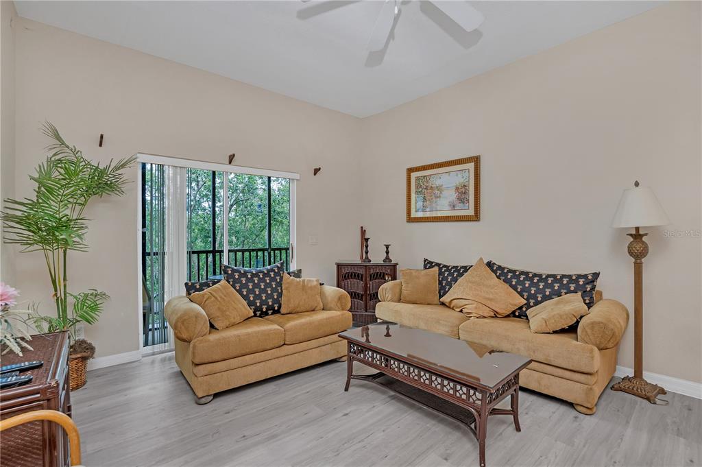 A living room features light-colored walls, gray wood-look flooring, two tan sofas, and a sliding glass door — 514 LUCAYA LOOP UNIT 514, DAVENPORT, FL