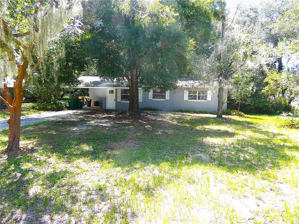A gray, single-story house with a concrete driveway, two doors, and a large green trash bin — 106 WILLARD AVENUE, FRUITLAND PARK, FL
